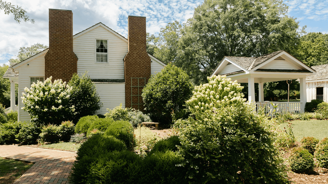 White home with two brick chimneys, surrounded by shrubs and bushes