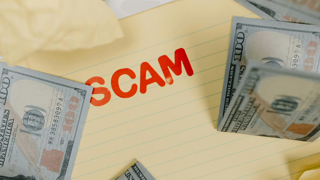 “Scam” written on yellow college-ruled paper, surrounded by $100 bills